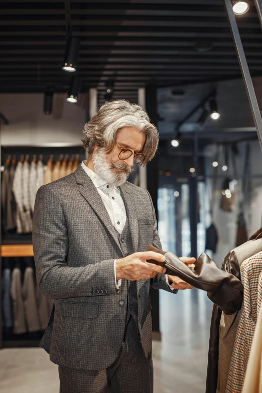 a man standing in front of a rack of clothes, wearing a suit and glasses, at checkout, gray beard, trending