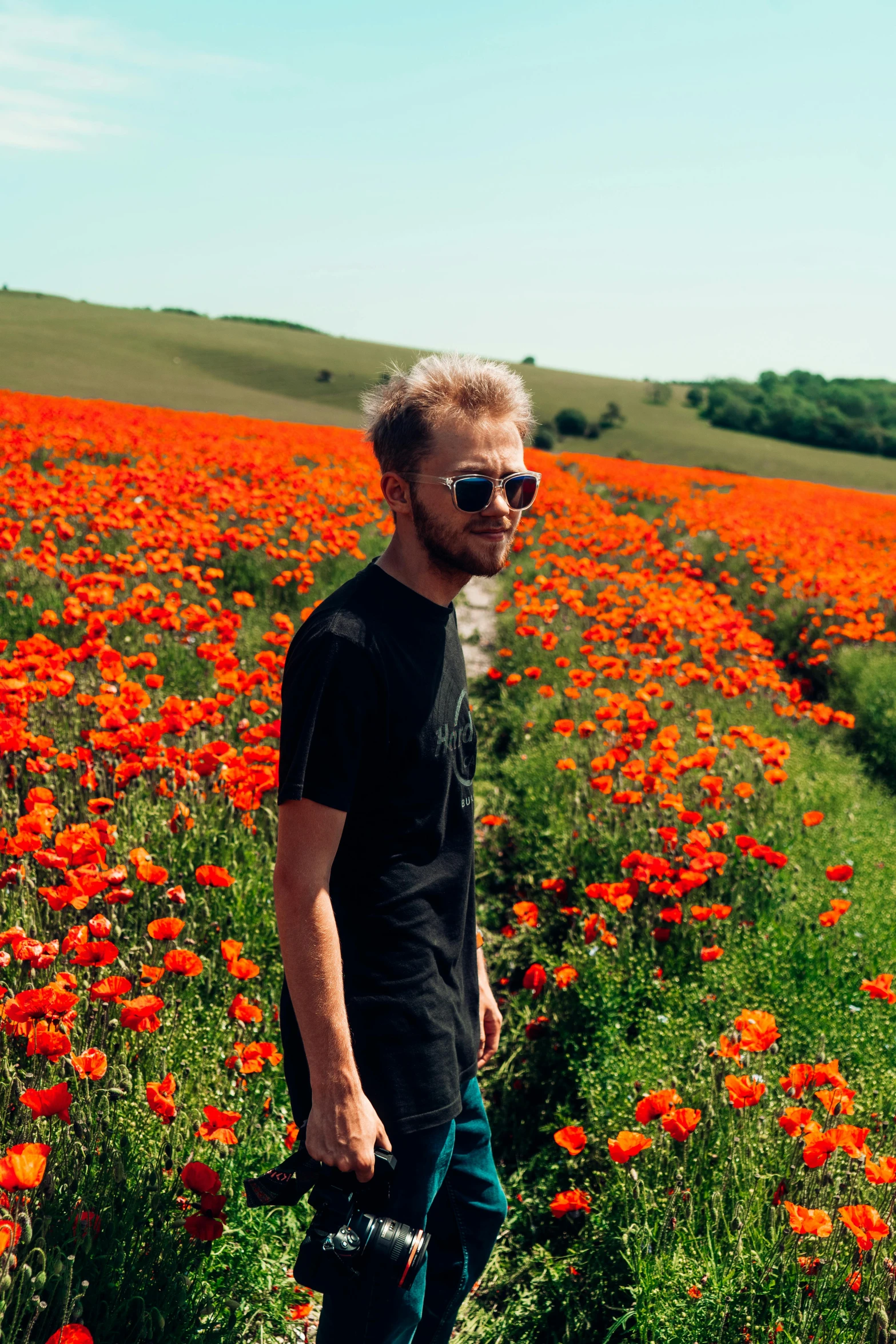 a man standing in a field of red flowers, by Julia Pishtar, color field, blonde british man, orange and black tones, instagram post, concert