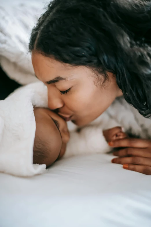 a woman kissing a baby on top of a bed, pexels contest winner, symbolism, laying down, diverse, medium head to shoulder shot, 1 4 9 3