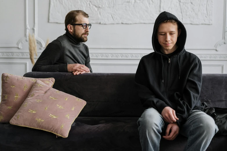 a man and a woman sitting on a couch, pexels, visual art, wearing a black hoodie, two young men, aged 13, emotional conflict