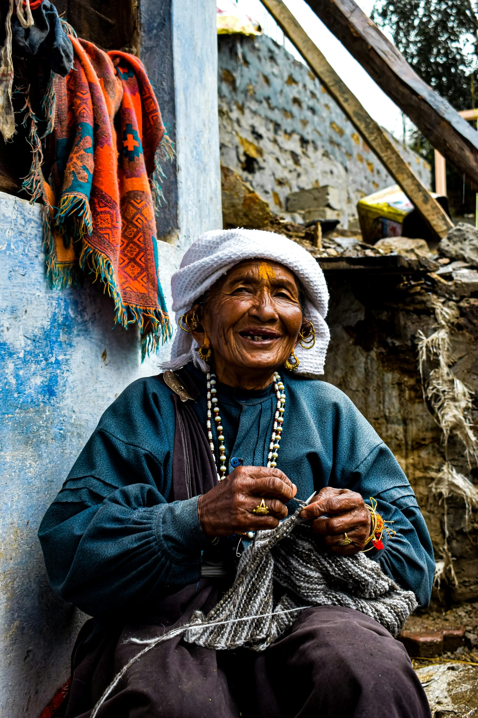 an old woman sitting in front of a building, an album cover, inspired by Steve McCurry, pexels contest winner, prayer flags, inca, made of wool, kind smile