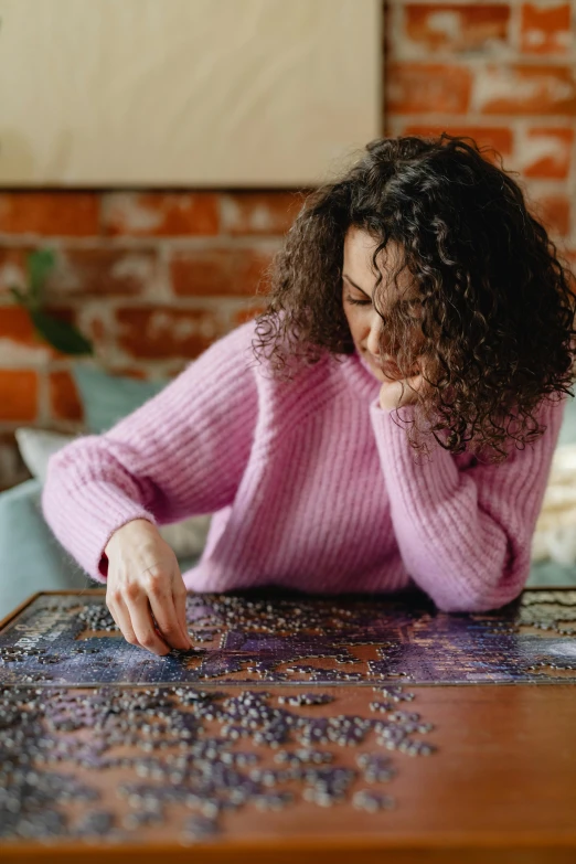 a woman sitting at a table with a puzzle, by Julia Pishtar, trending on pexels, wearing a purple sweatsuit, intricately detailed, brunette, precious moments