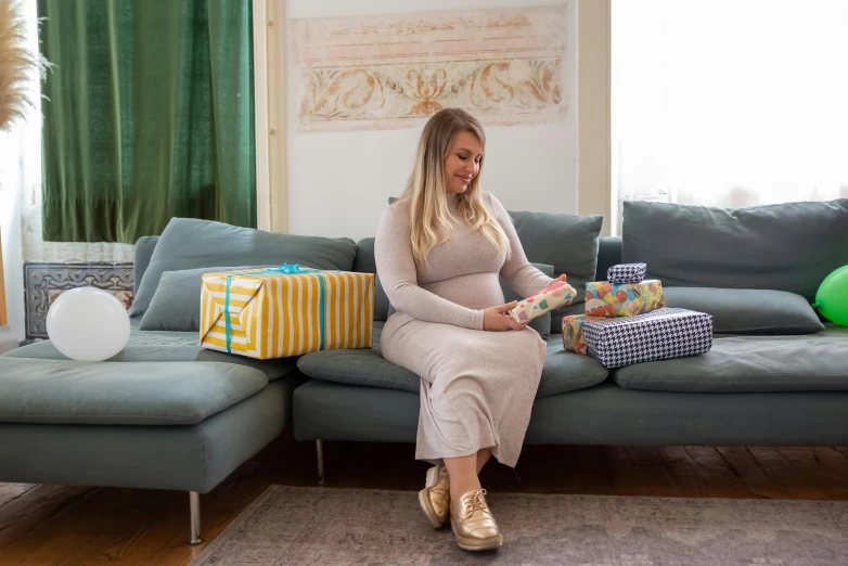 a woman sitting on a couch reading a book, an album cover, pexels contest winner, happening, pregnant belly, birthday wrapped presents, morandi colour scheme, plus-sized