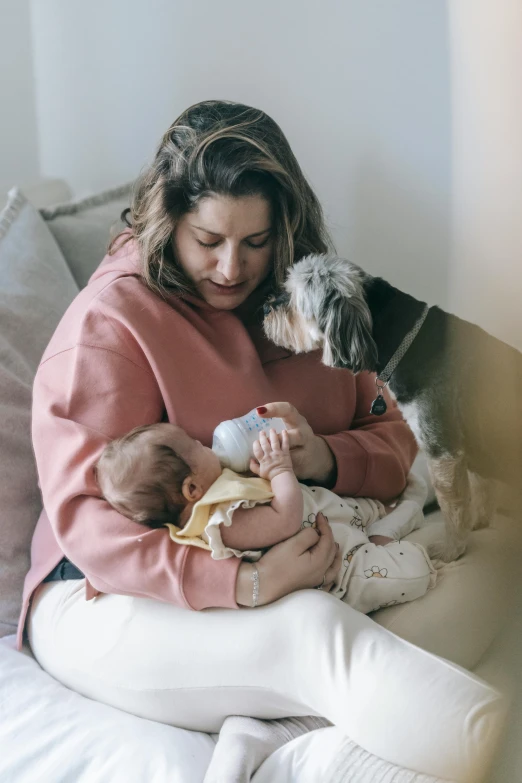 a woman sitting on a bed holding a baby and a dog, pexels contest winner, renaissance, wearing a pastel pink hoodie, milk, eating, profile image
