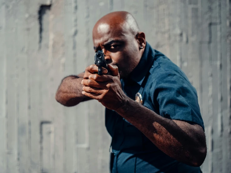 a man in a blue shirt holding a gun, pexels contest winner, huell babineaux, cop, super focused, chunky build