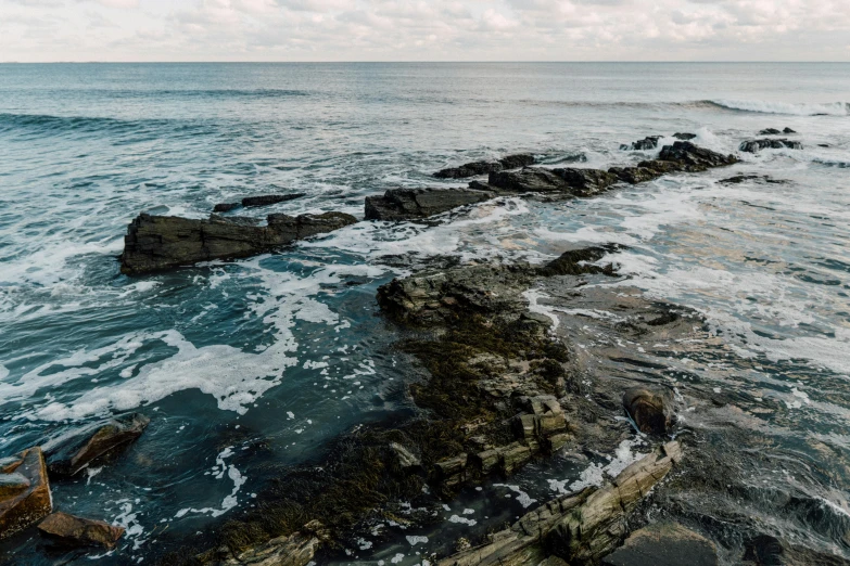 a man standing on top of a rock next to the ocean, inspired by Elsa Bleda, unsplash, minimalism, rocky roads, marsden, detailed water, panoramic shot