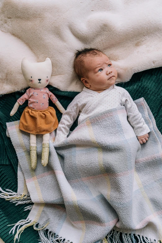 a baby laying on top of a blanket next to a stuffed animal, by Alice Mason, designed for cozy aesthetics!, standing, mini model, light grey blue and golden