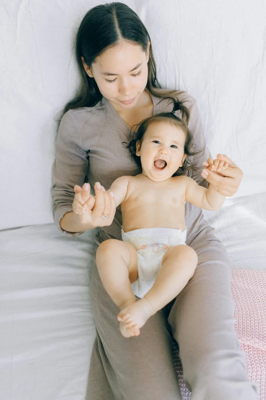 a woman sitting on top of a bed holding a baby, pexels contest winner, soft volume absorbation, walking towards camera, her tiny hands are on her thighs, asian