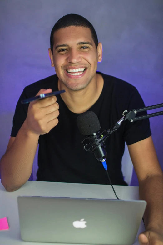 a man sitting in front of a laptop computer, an album cover, inspired by Randy Vargas, featured on reddit, happening, smiling into the camera, holding microphone, he is wearing a black t-shirt, smol