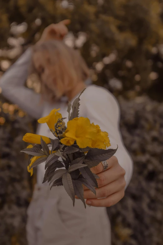 a woman holding a bunch of yellow flowers, inspired by Elsa Bleda, trending on unsplash, romanticism, grey, golden hour cinematic, background image, low quality photo