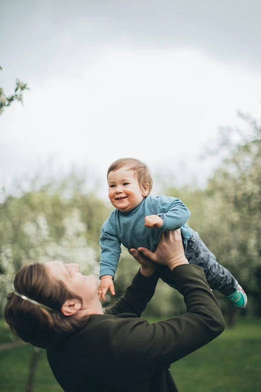 a woman holding a baby up in the air, pexels contest winner, in the garden, a handsome, in the countryside, thumbnail