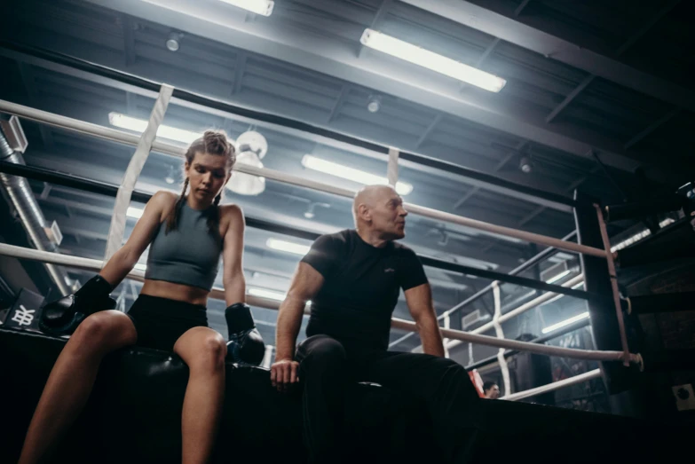 a man and a woman sitting in a boxing ring, local gym, ellie victoria gale, toned down, thumbnail