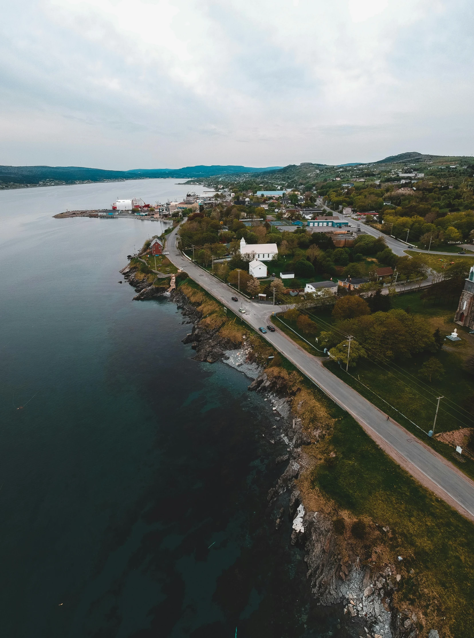 a road that is next to a body of water, a portrait, drone photo, in the foreground a small town, francois legault, 4k image”