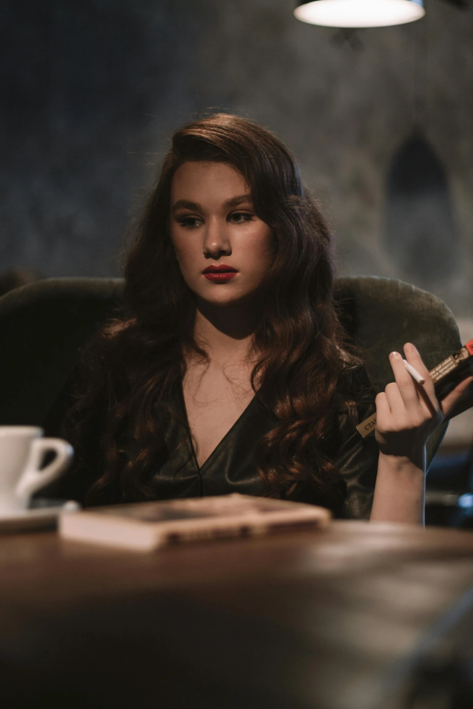 a woman sitting at a table with a cigar in her hand, a portrait, inspired by Nan Goldin, trending on pexels, renaissance, hailee steinfeld, dark angel of coffee, holding wand, amy sol in the style of