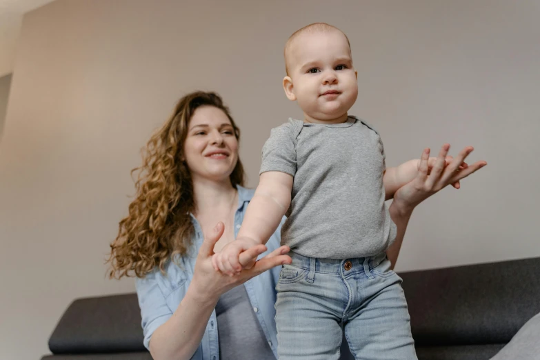 a woman sitting on a couch holding a baby, pexels contest winner, antipodeans, standing on two legs, avatar image, wearing a shirt and a jean, spinning hands and feet