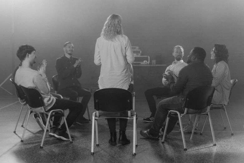 a group of people sitting around each other in chairs, a black and white photo, pexels, casting a protection spell, presentation, worship, performing a music video