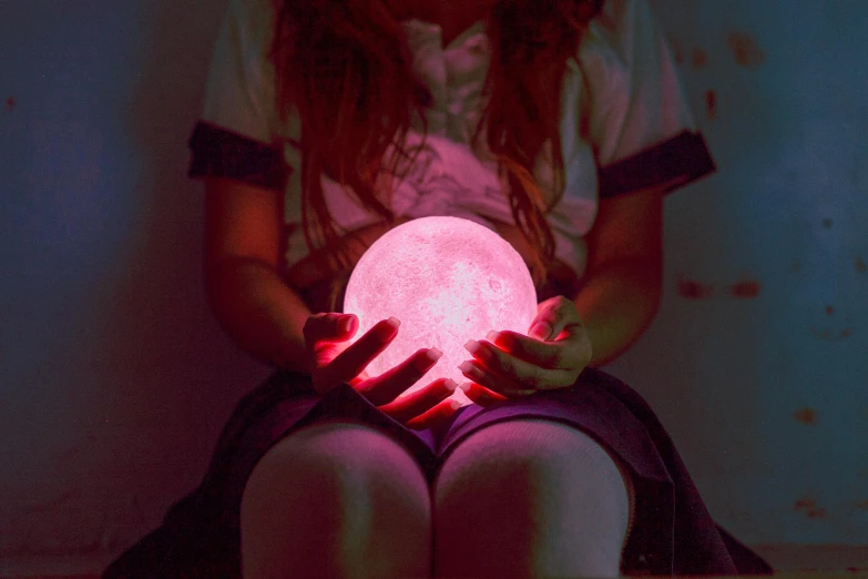 a girl holding a glowing ball in her hands, trending on pexels, pink moon, made of crystal, sitting down, mood light