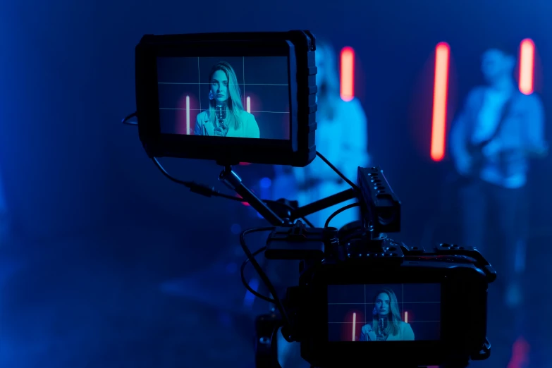 a video camera in front of a group of people, inspired by Elsa Bleda, shutterstock, video art, blue and red lighting, female model, neon operator margot robbie, general studio lighting