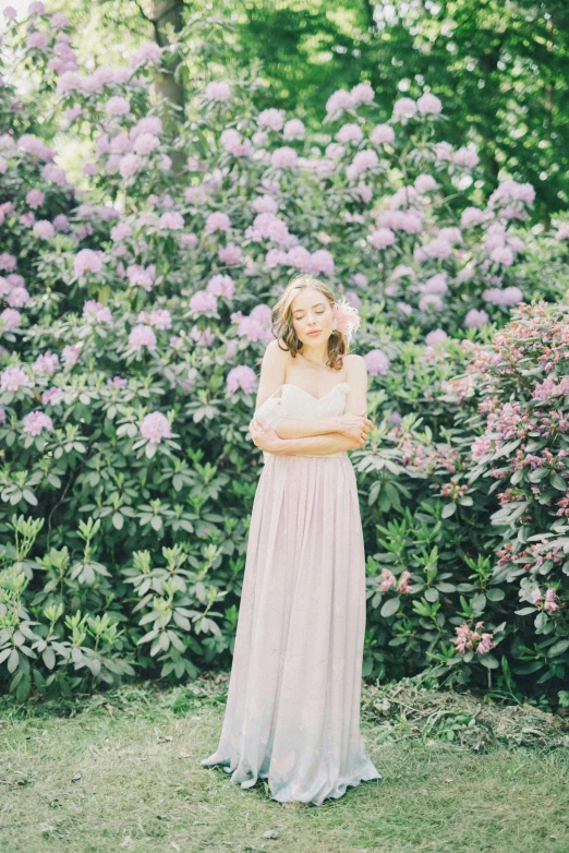 a woman standing in front of a bush of purple flowers, inspired by Oleg Oprisco, unsplash, wedding photo, grey, medium format. soft light, may)