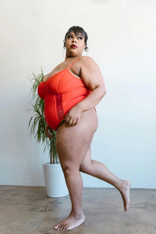 a woman in an orange top standing next to a potted plant, unsplash, red body suit, bbw, is wearing a swimsuit, profile image