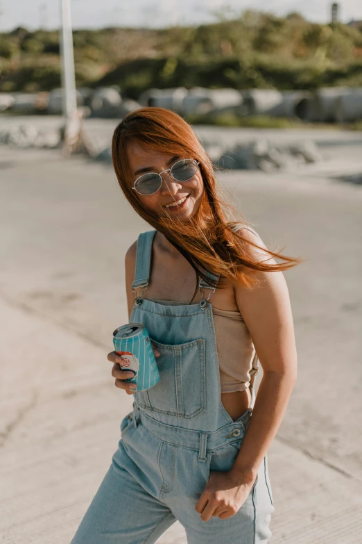 a woman standing on the side of a road holding a drink, trending on pexels, happening, blue overalls, wearing : tanktop, ( redhead, malaysian