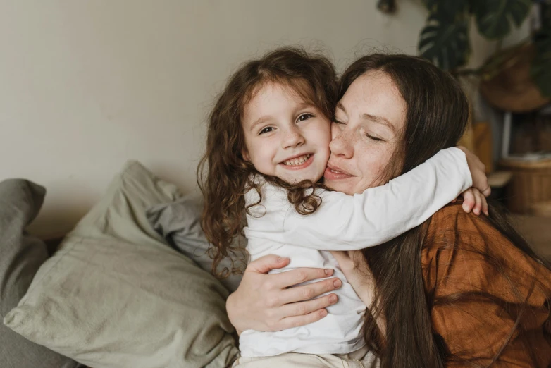 a woman sitting on top of a couch next to a little girl, pexels contest winner, hugging each other, avatar image, girl with brown hair, manuka