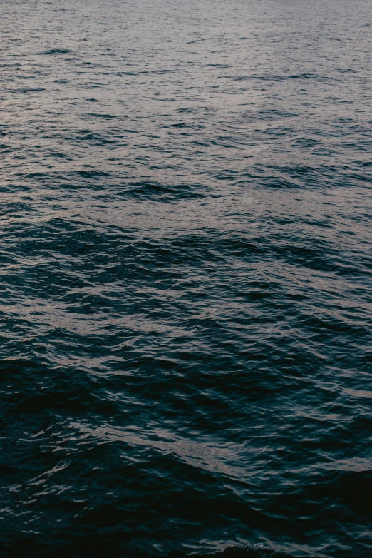 a large body of water with a boat in the distance, an album cover, by Elsa Bleda, unsplash, happening, dark ocean water, wavy, navy, ignant