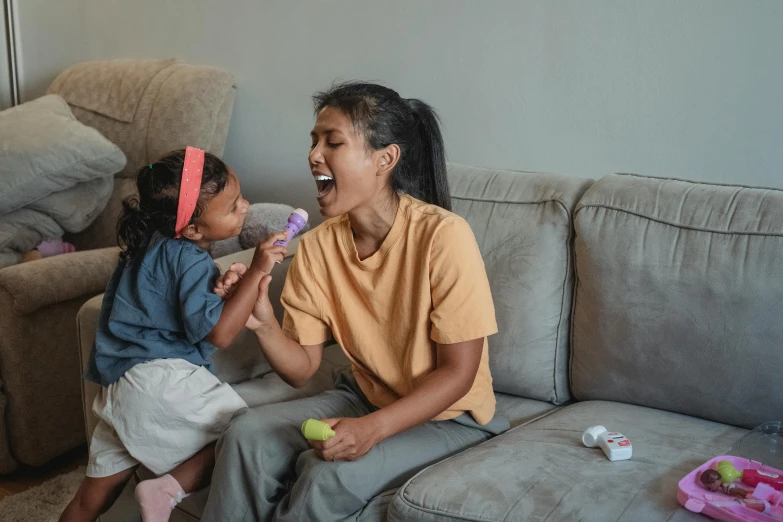 a woman and a little girl sitting on a couch, pexels contest winner, happening, open happy mouth, toothpaste blast, indian girl with brown skin, holding maracas