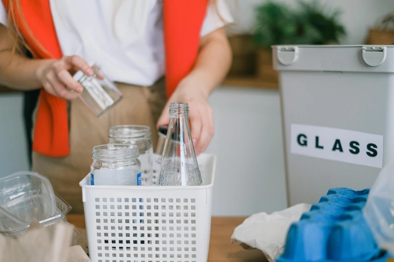 a woman standing in front of a container filled with bottles, pexels contest winner, clean and simple, hand on table, recycled, grey