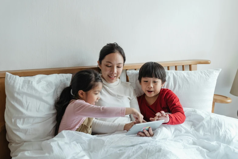 a woman and two children sitting on a bed, a cartoon, pexels, an asian woman, everything fits on the screen, on the bed, english