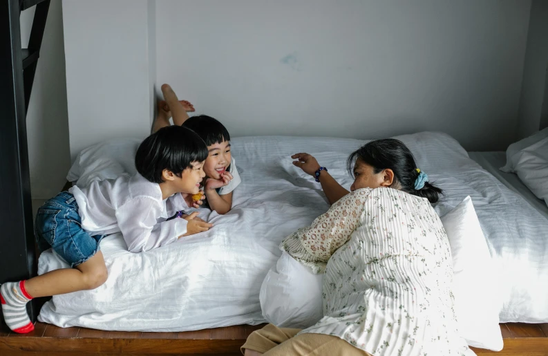 a couple of kids laying on top of a bed, pexels contest winner, asian women, with a kid, reaching out to each other, profile image