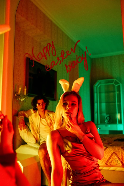 a woman sitting on top of a bed next to a man, an album cover, inspired by David LaChapelle, pop art, bunnies, red lighting on their faces, holding easter eggs, sydney sweeney