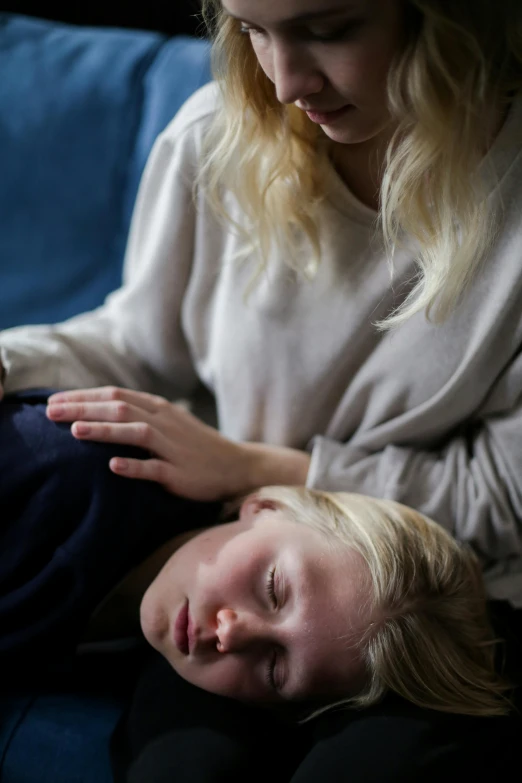 a woman sitting on top of a blue couch next to a child, unsplash, portrait of a woman sleeping, blond boy, head down, hammershøi