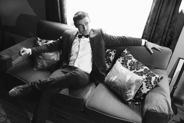 a man sitting on a couch talking on a cell phone, a black and white photo, by Emma Andijewska, renaissance, formal suit, taron egerton as wolverine, relaxed pose, black tie