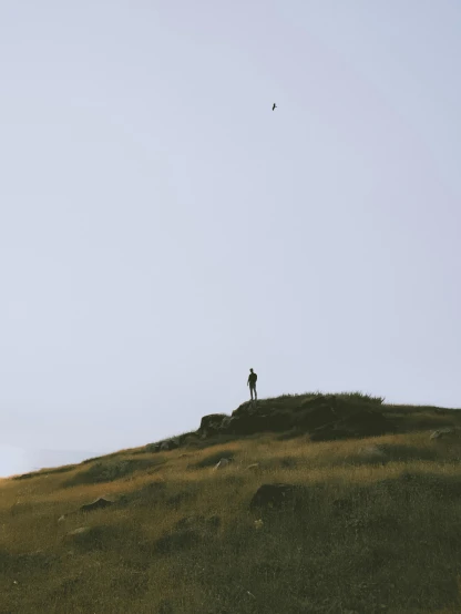 a person standing on top of a hill flying a kite, by Attila Meszlenyi, postminimalism, an icelandic landscape, bird sight, small stature, alessio albi