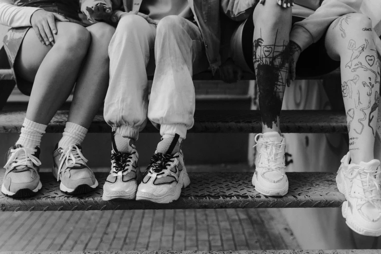 a group of people sitting next to each other on a bench, a black and white photo, pexels, graffiti, sneaker design, close-up on legs, standing on a ladder, growth of a couple