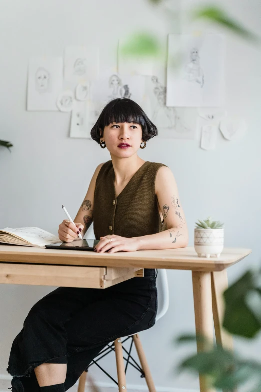 a woman sitting at a desk writing in a notebook, a portrait, inspired by Ruth Jên, trending on pexels, tattooed, standing on a desk, ruan jia and joao ruas, architect