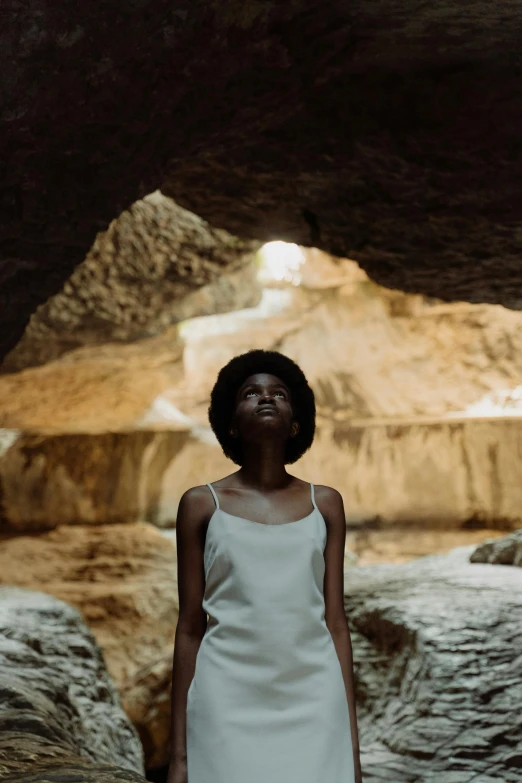 a woman in a white dress standing in a cave, inspired by Gordon Parks, afrofuturism, 2019 trending photo, light skinned african young girl, ignant, low sun