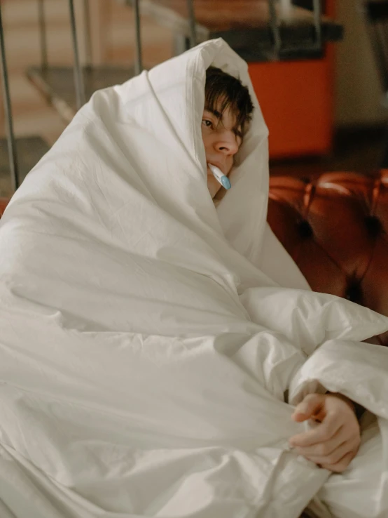 a man sitting on a couch covered in a blanket, inspired by Elsa Bleda, pexels contest winner, happening, white puffy outfit, with a cigarette in its mouth, while posing in the same bed, cloak covering face