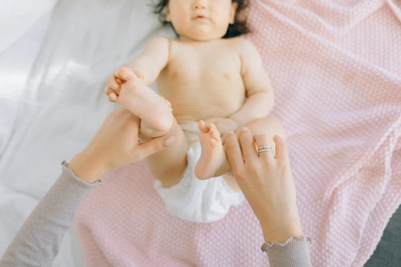 a woman holding a baby on top of a bed, trending on pexels, the forefoot to make a v gesture, high - angle view, bare leg, white and pink cloth