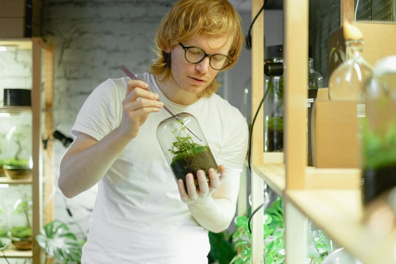 a woman standing in front of a shelf filled with plants, inside a glass jar, protophyta, bo burnham, plating