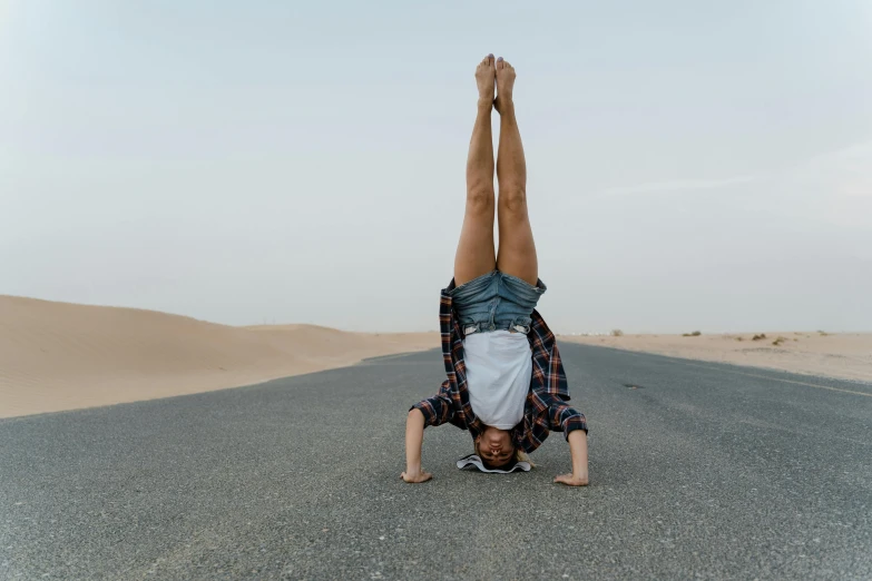 a man doing a handstand in the middle of the road, pexels contest winner, arabesque, standing in a desert, an ahoge stands up on her head, lying down, plain background