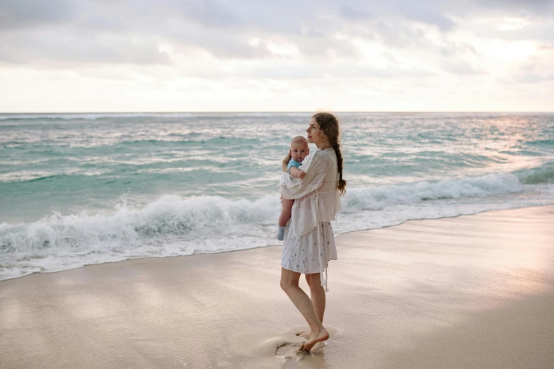 a woman holding a baby on a beach, pexels contest winner, renaissance, wearing a simple robe, australian beach, thumbnail, walking