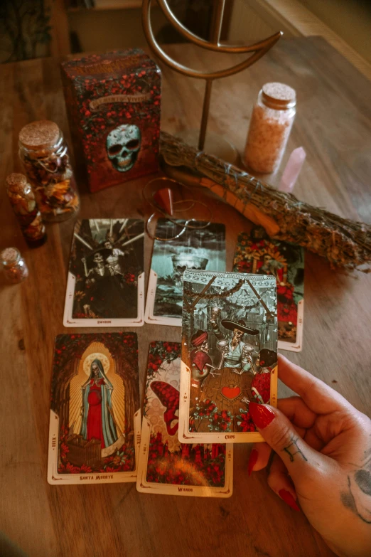 a person holding several tarot cards on a table, poster art, witch hut, sacred skulls, slide show, grainy