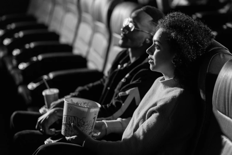 a couple of people sitting next to each other, a black and white photo, by Adam Marczyński, pexels, popcorn as morpheus, customers, black people, warmly lit