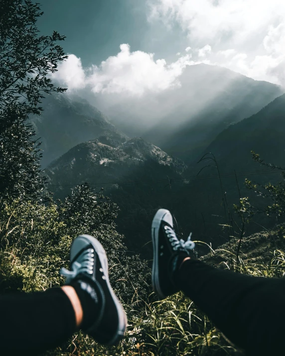 a person sitting on top of a lush green hillside, a picture, trending on unsplash, sneaker photo, cloud forest in background, view from below, multiple stories