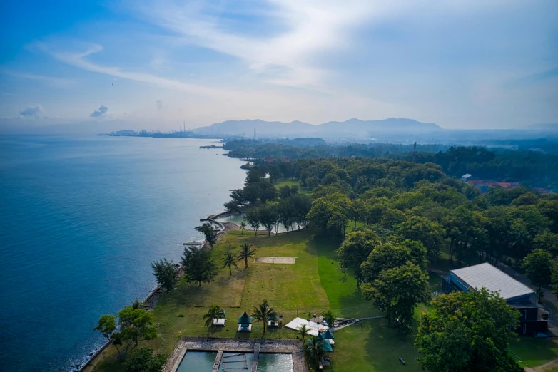 a large body of water next to a lush green field, by Bernardino Mei, pexels contest winner, happening, tropical coastal city, sangyeob park, golf course in background, malaysian