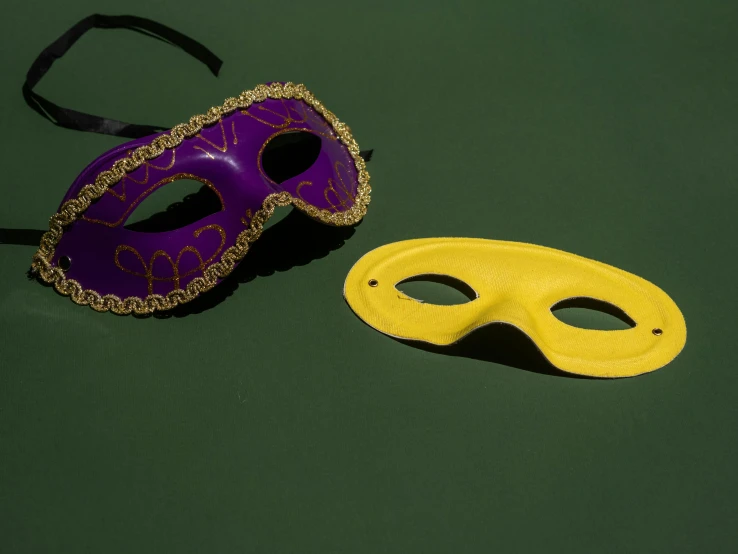 two masks sitting next to each other on a table, by Carey Morris, trending on pexels, yellow purple green, tournament, eye patch, composite