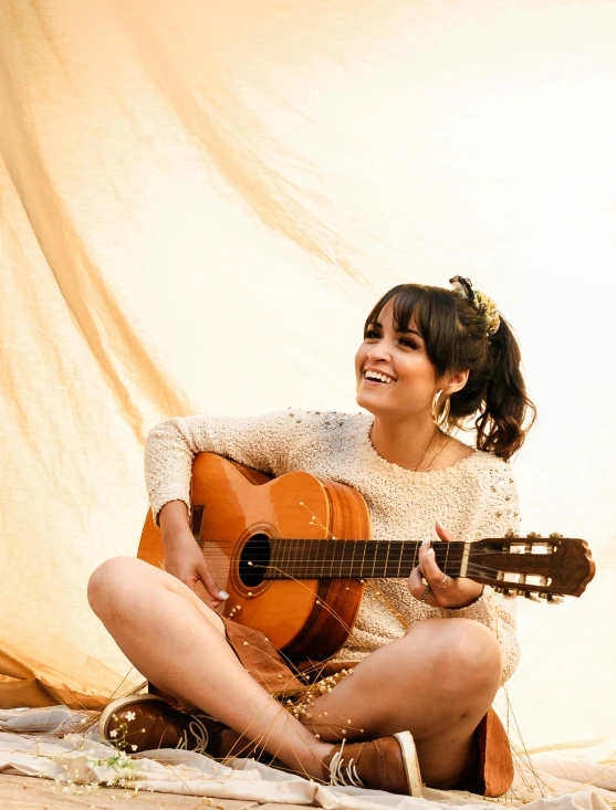 a woman sitting on the ground playing a guitar, an album cover, inspired by Glòria Muñoz, pexels contest winner, arabesque, smiling slightly, boke, isabela moner, profile image