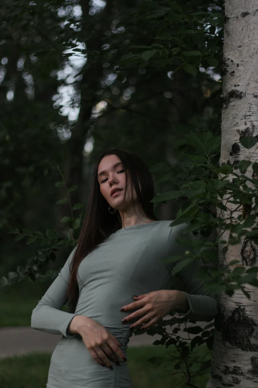 a woman leaning against a tree in a forest, an album cover, inspired by Elsa Bleda, pexels contest winner, realism, pregnant belly, bella poarch, wearing a green sweater, russian girlfriend